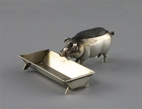 An Edwardian novelty silver pin cushion, modelled as a pig at a trough, by Adie & Lovekin, Birmingham, 1907, trough 56mm.